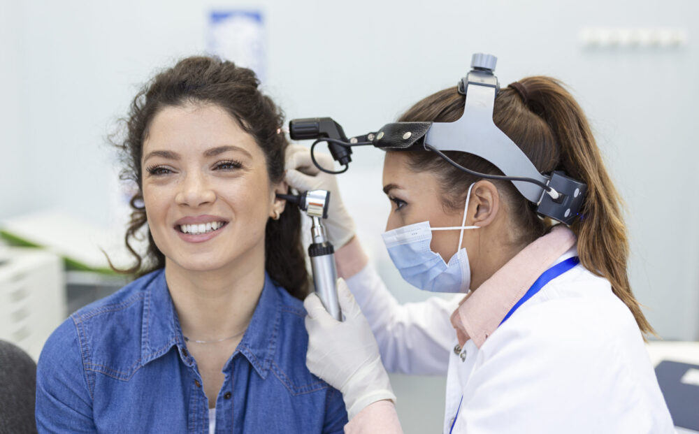 Hearing exam. Otolaryngologist doctor checking woman's ear using otoscope or auriscope at medical clinic.